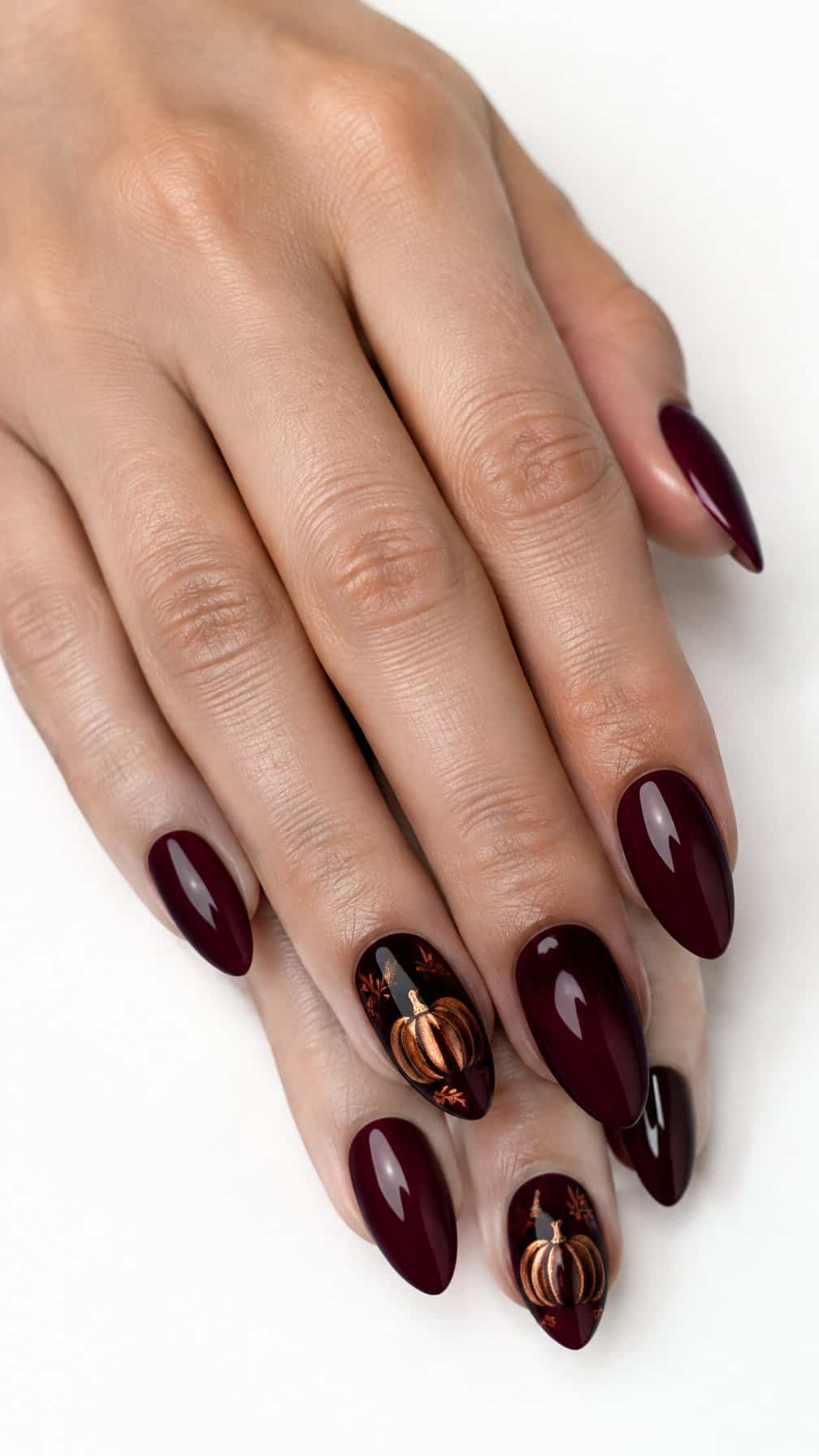 Glossy burgundy nails featuring copper pumpkin designs
