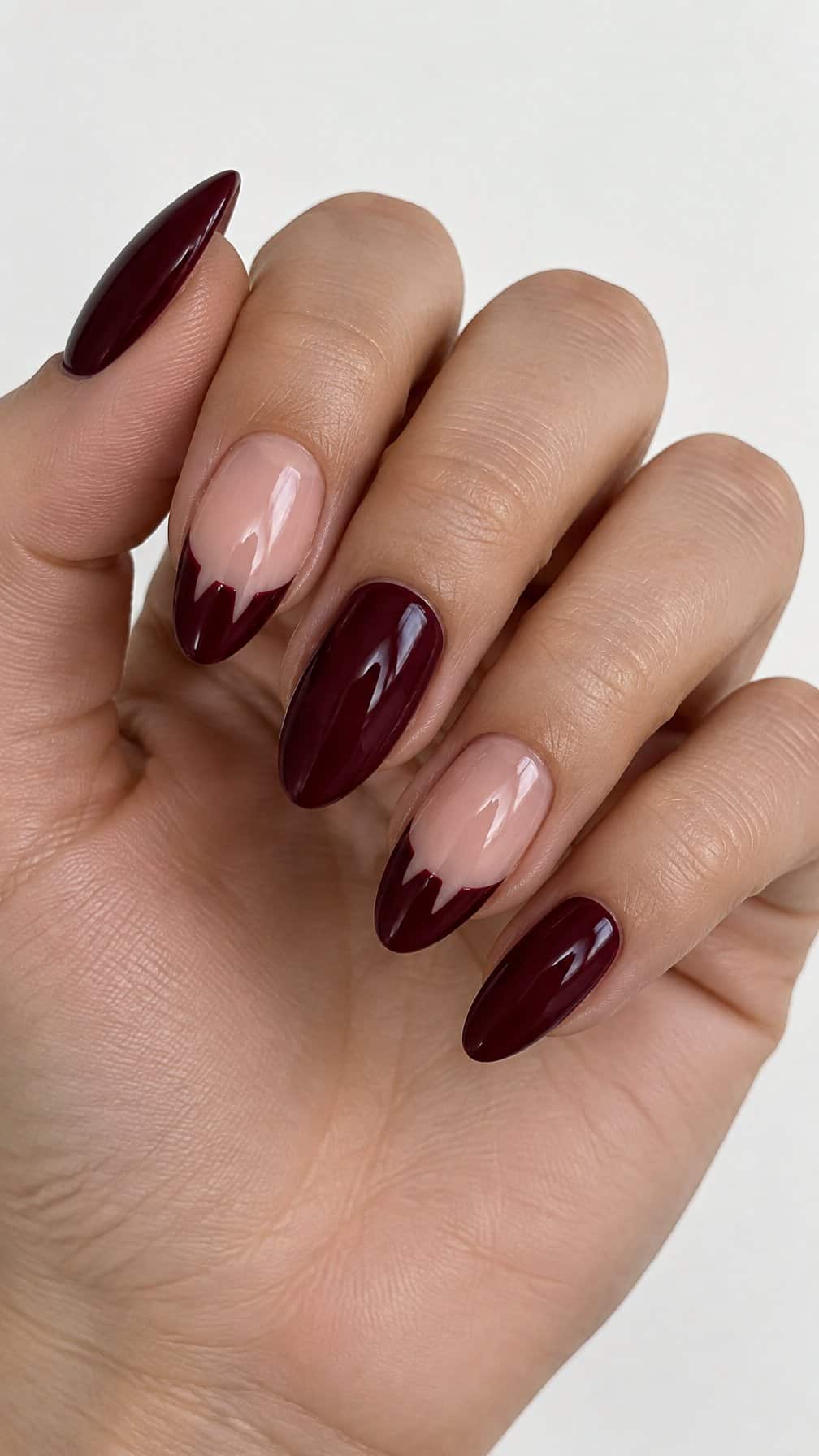 Glossy burgundy French-tip nails featuring small vampire-bite shapes and several solid burgundy nails