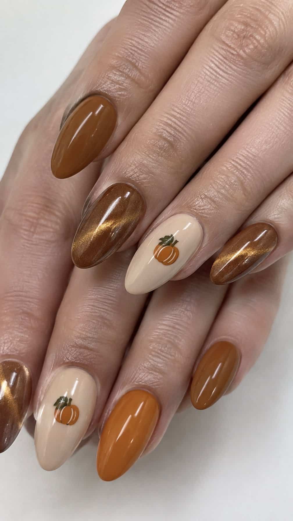 Glossy caramel, orange, and beige nails decorated with small pumpkin designs