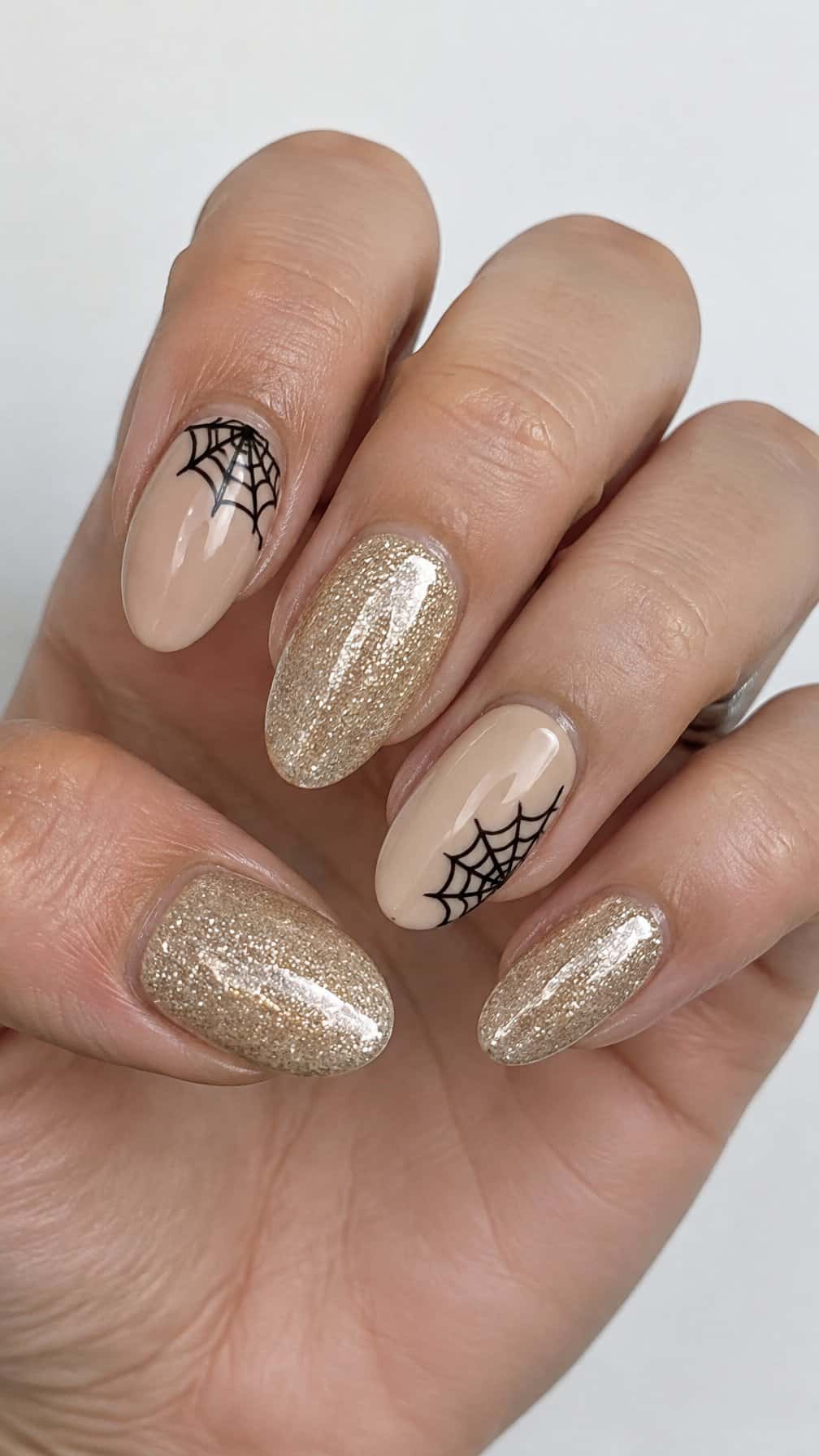 Glossy champagne glitter and nude gel nails, featuring black spider-web designs on several nails