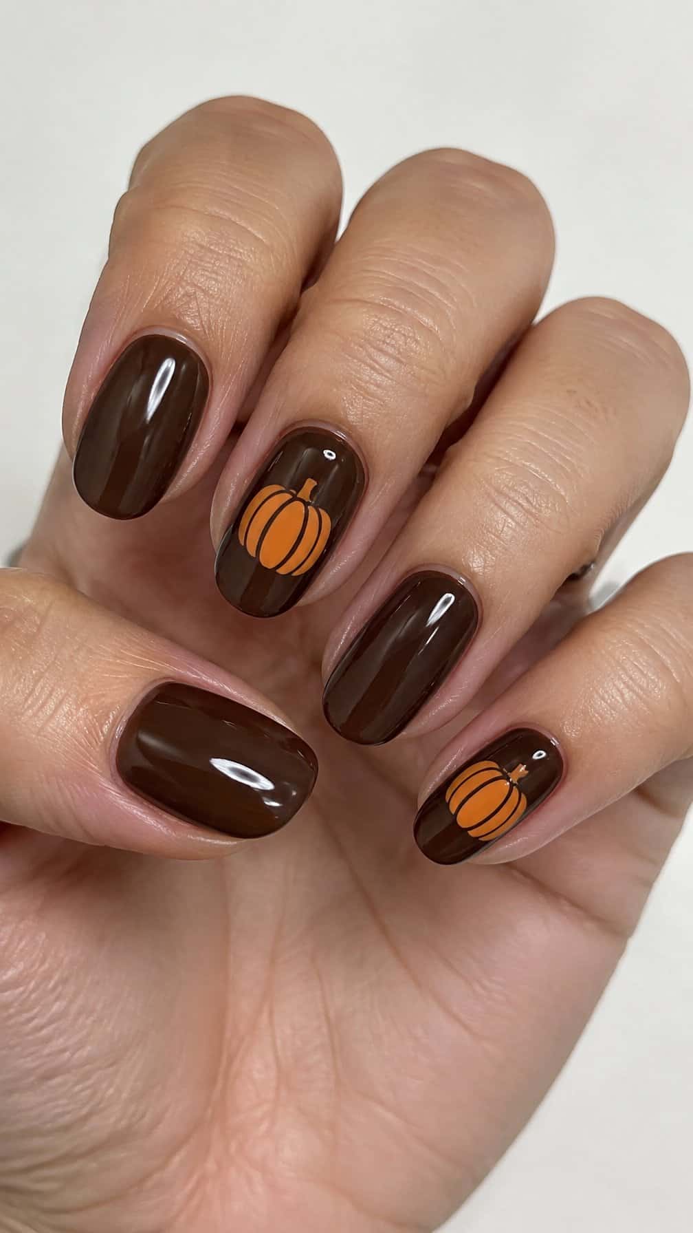 Glossy chocolate brown nails and small orange pumpkin designs on a few accent nails
