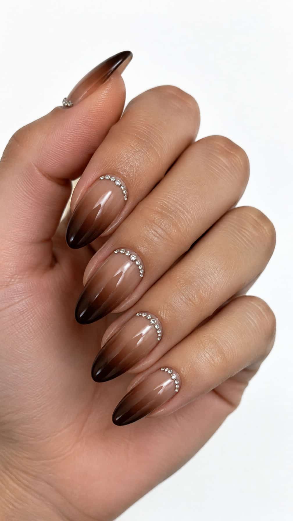 Glossy chocolate brown ombre nails decorated with small rhinestones around the cuticles, photographed