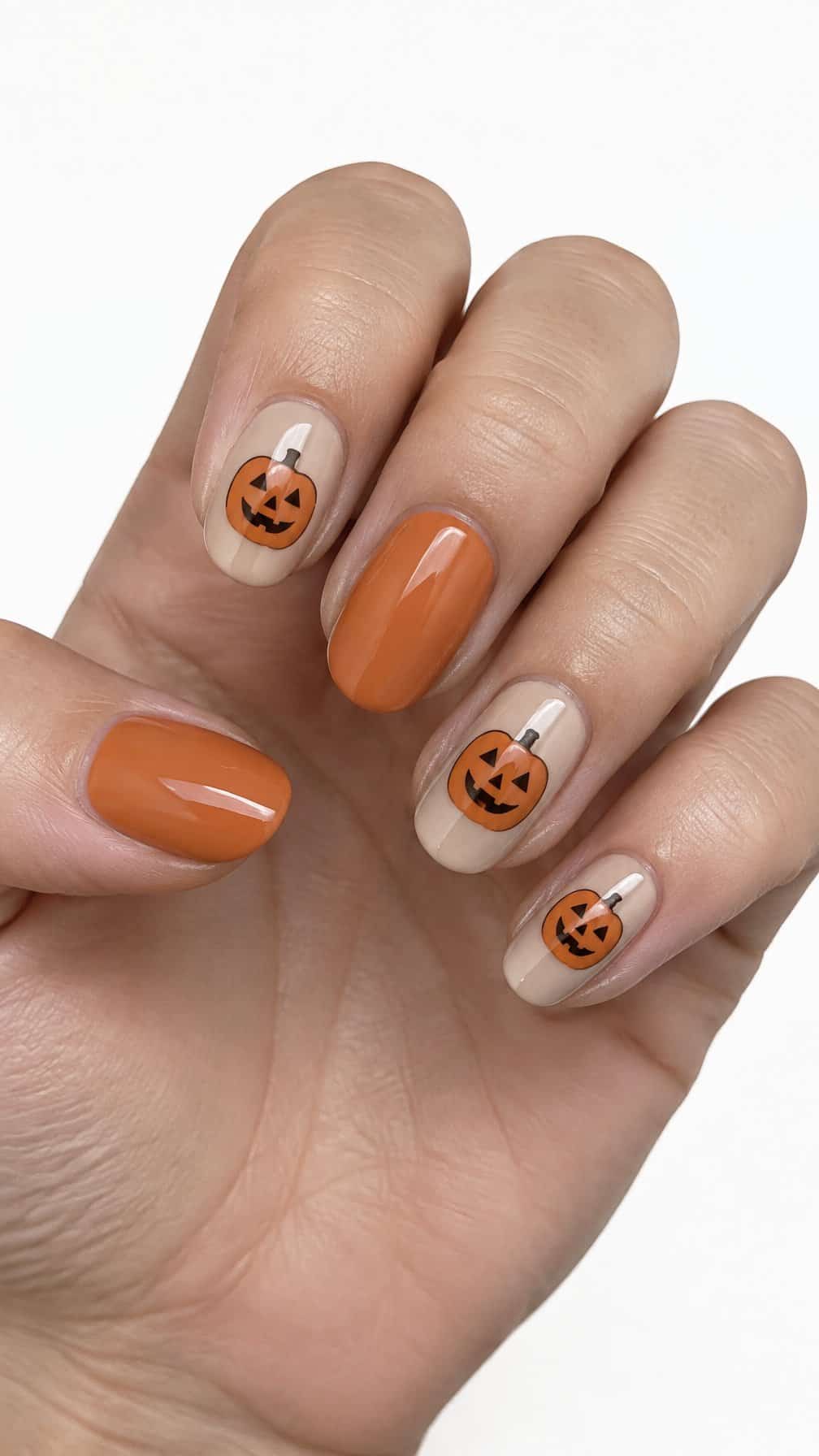 Nude glossy nails featuring simple orange jack-o'-lantern faces