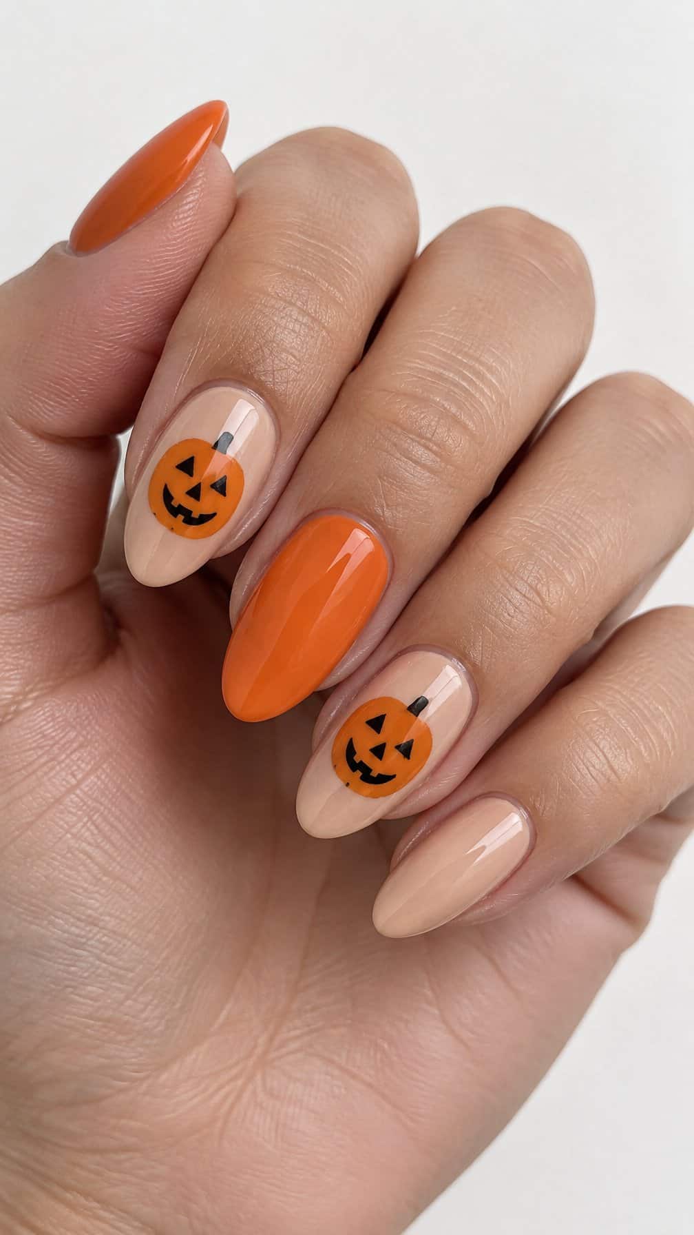 Glossy nude and orange nails decorated with simple jack-o'-lantern faces