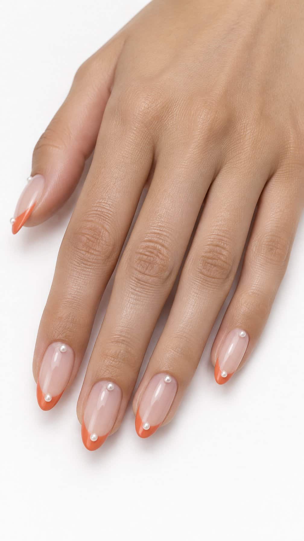 Coral orange French-tip nails and small pearl accents rests