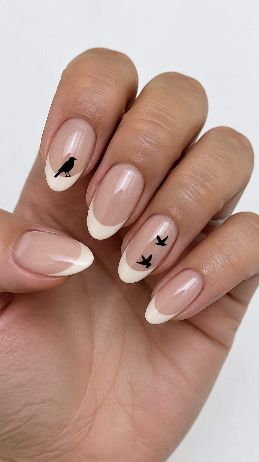Creamy French-tip nails and tiny black crow designs on a few nails