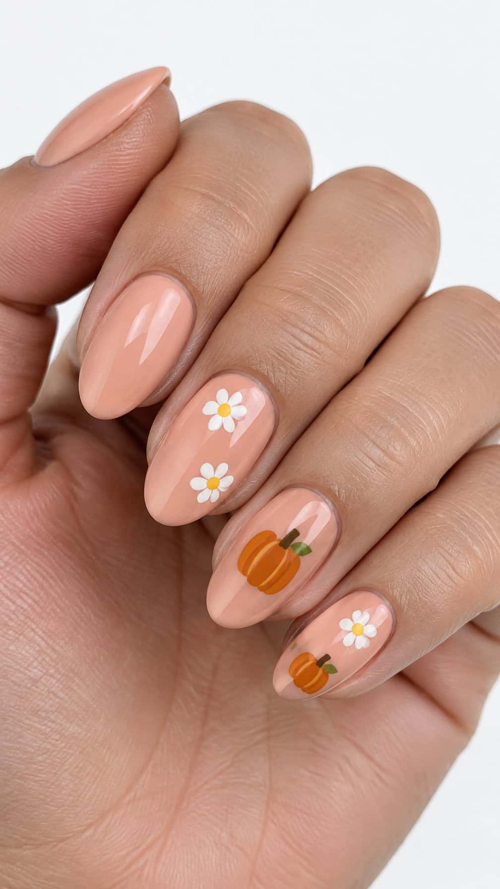 Glossy peach nails decorated with small white daisies and orange pumpkins