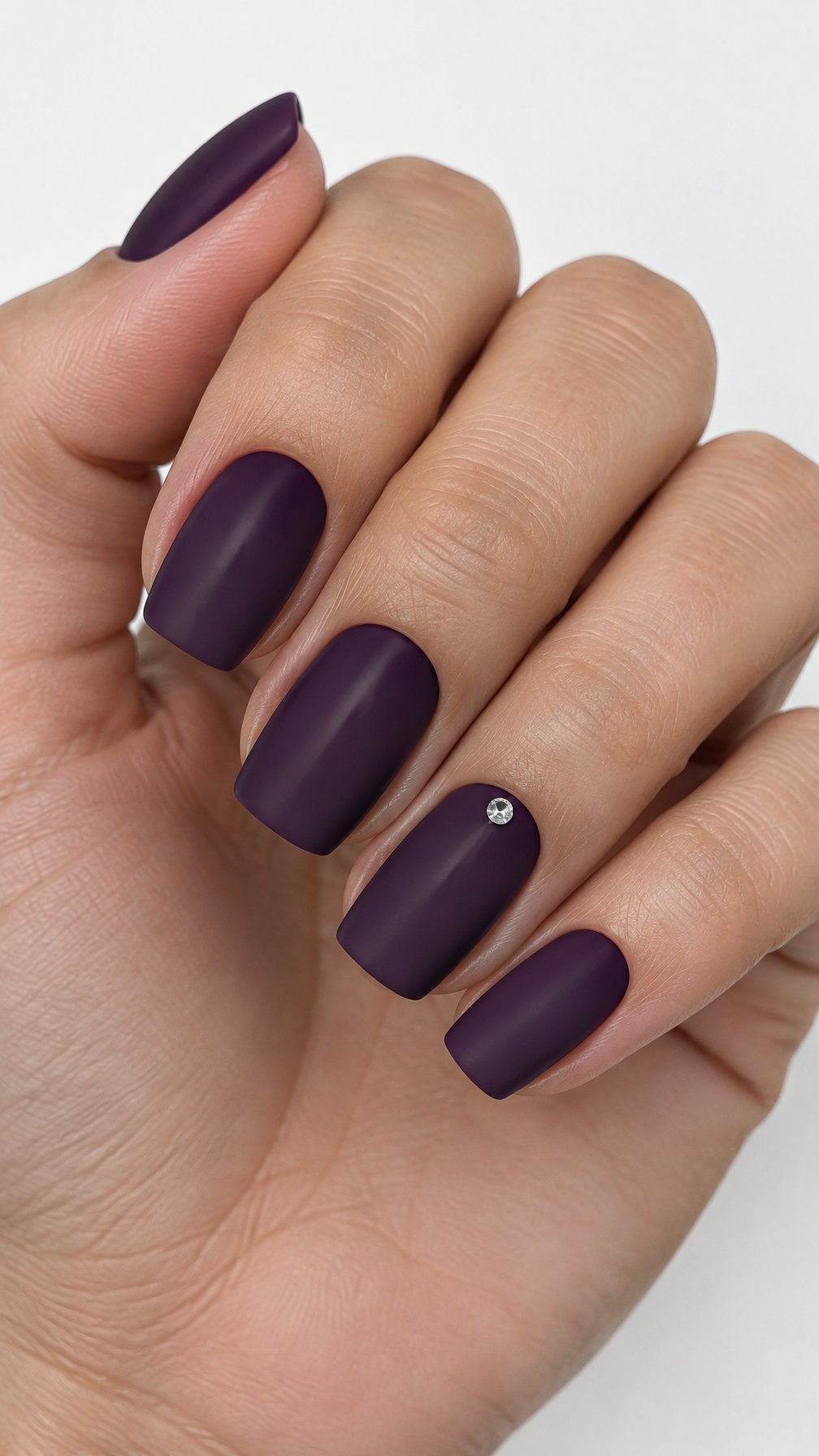 Matte deep purple manicured nails and a single rhinestone accent