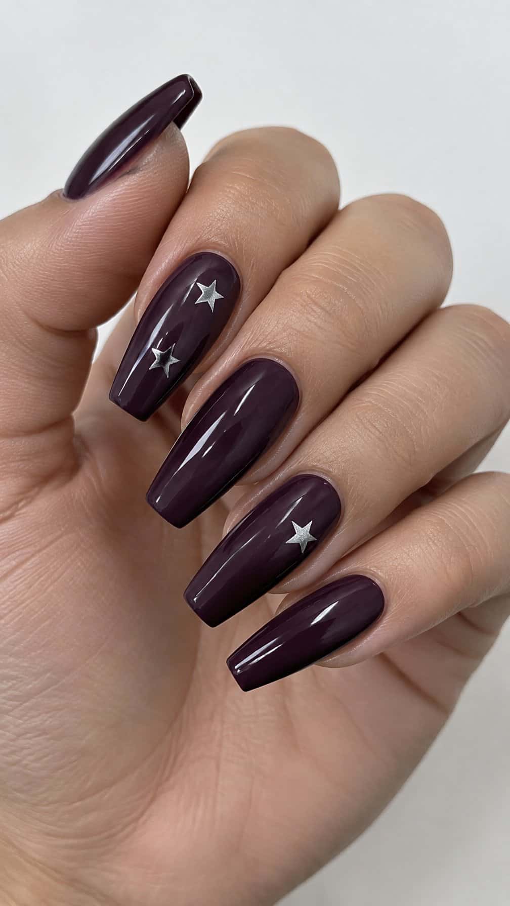Glossy deep plum coffin-shaped nails decorated with small silver stars