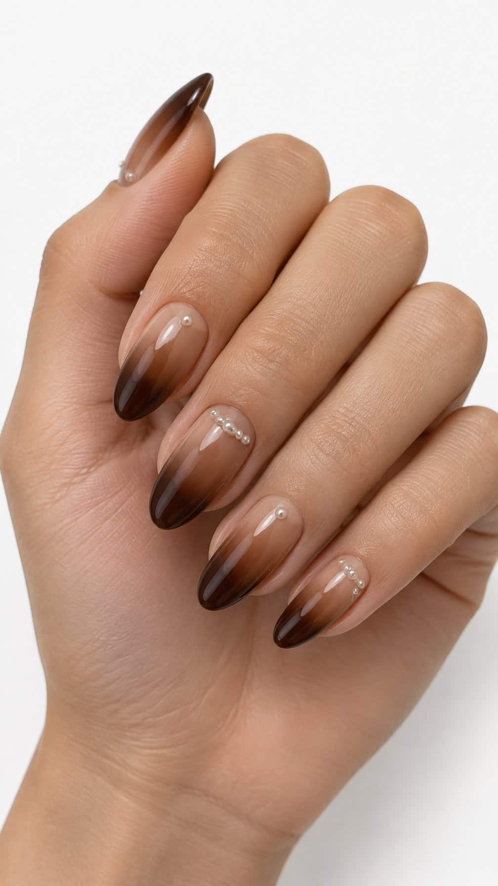 Glossy almond-shaped nails with brown ombré coloring and tiny pearl accents