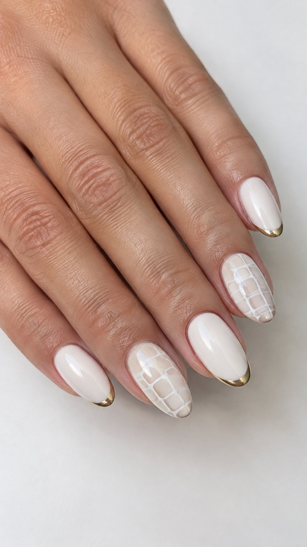 A glossy white manicure with gold-tipped nails and subtle crocodile-pattern details