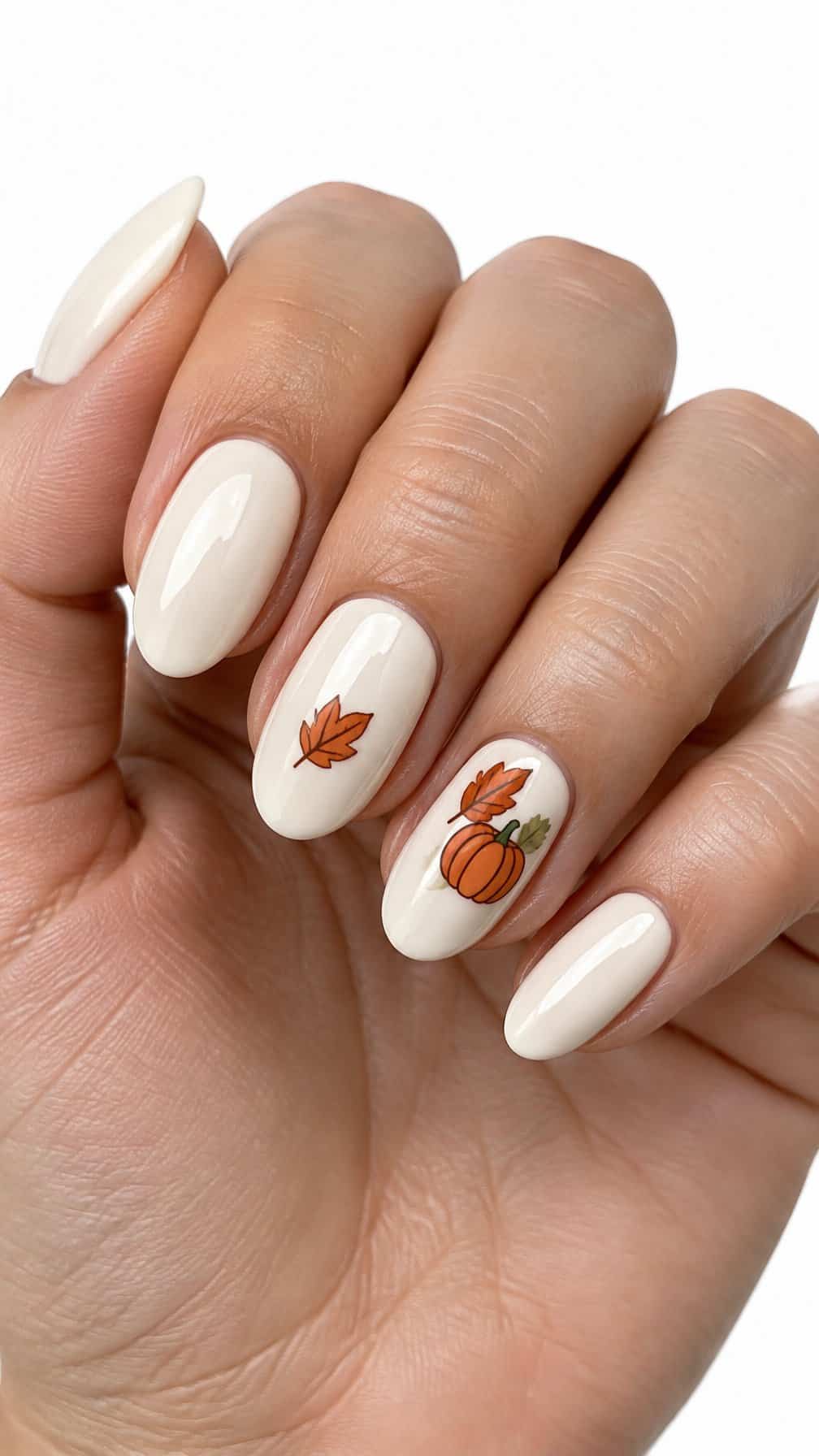Glossy ivory nails decorated with small orange pumpkins and autumn leaves