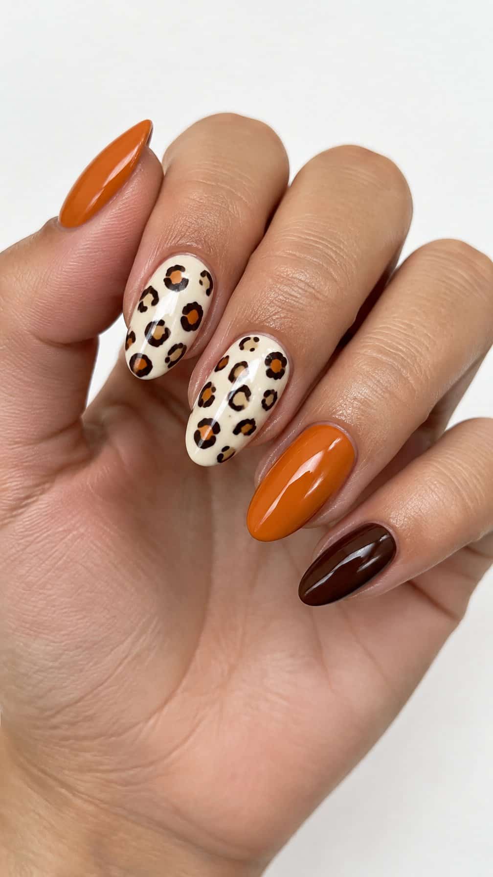 Glossy pumpkin-orange, brown, ivory, and leopard-print manicure