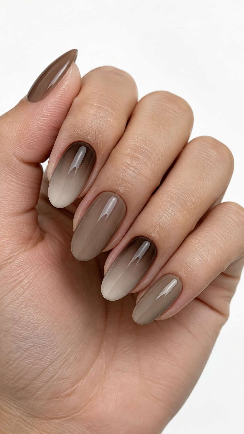 A close-up photograph of one hand with glossy brown ombre manicured nails