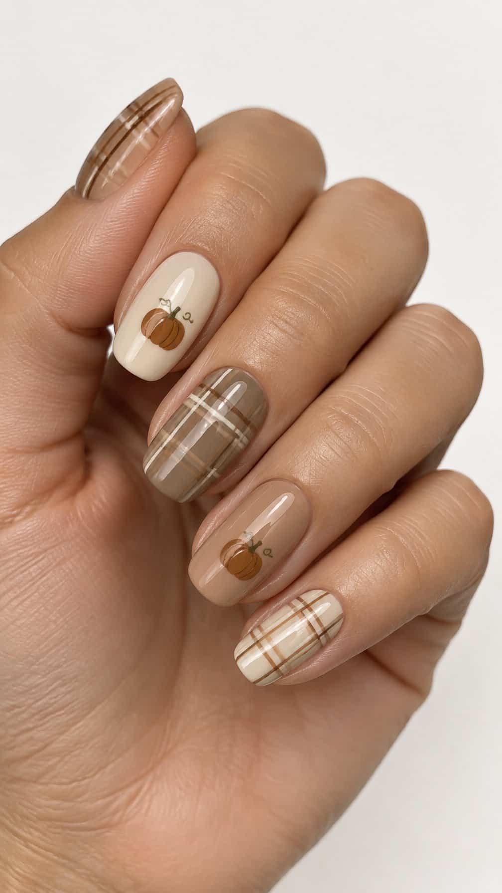 Neutral plaid manicured nails with small orange pumpkin designs