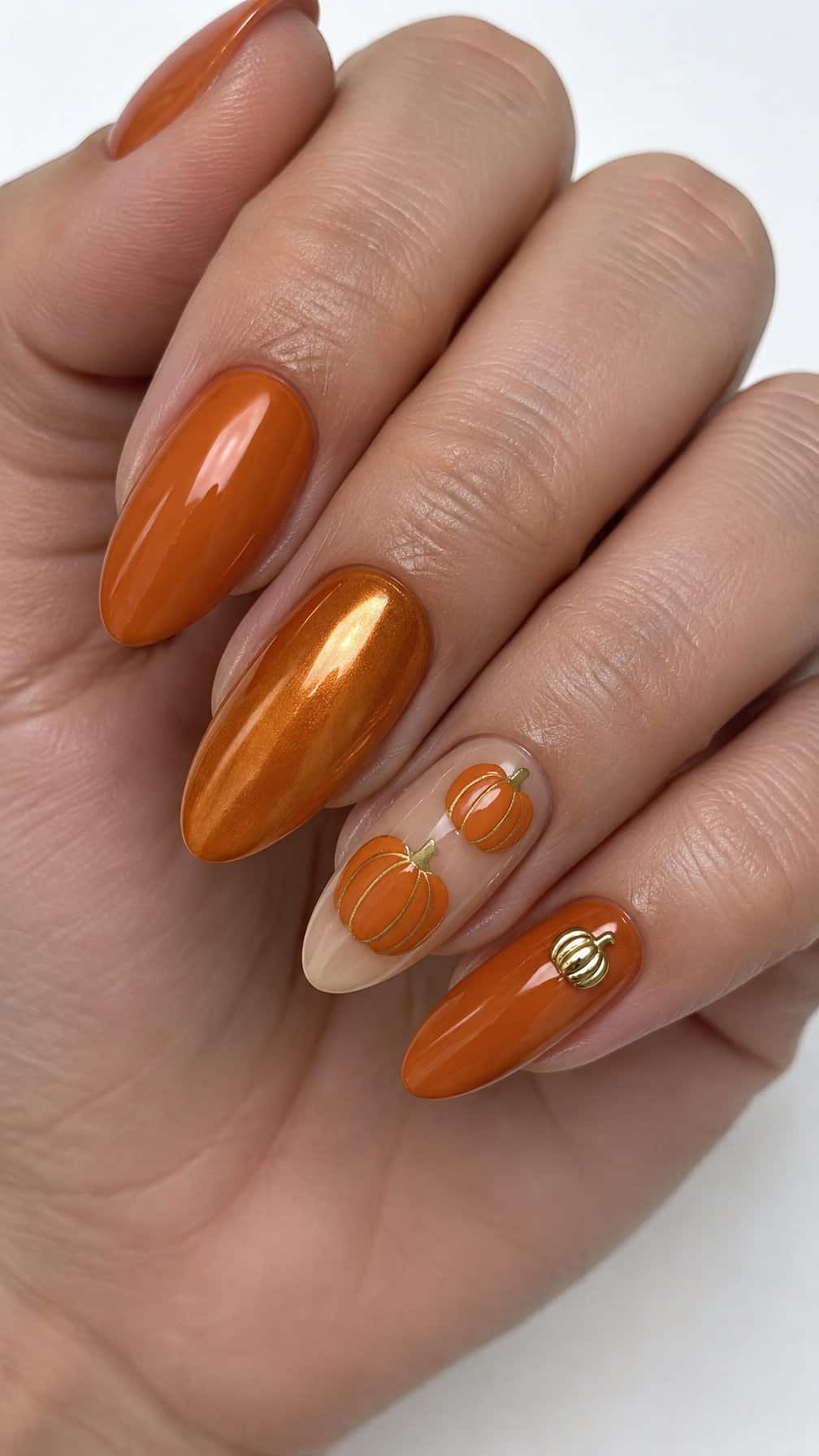 Glossy orange manicure, pumpkin nail art, and small gold pumpkin accents