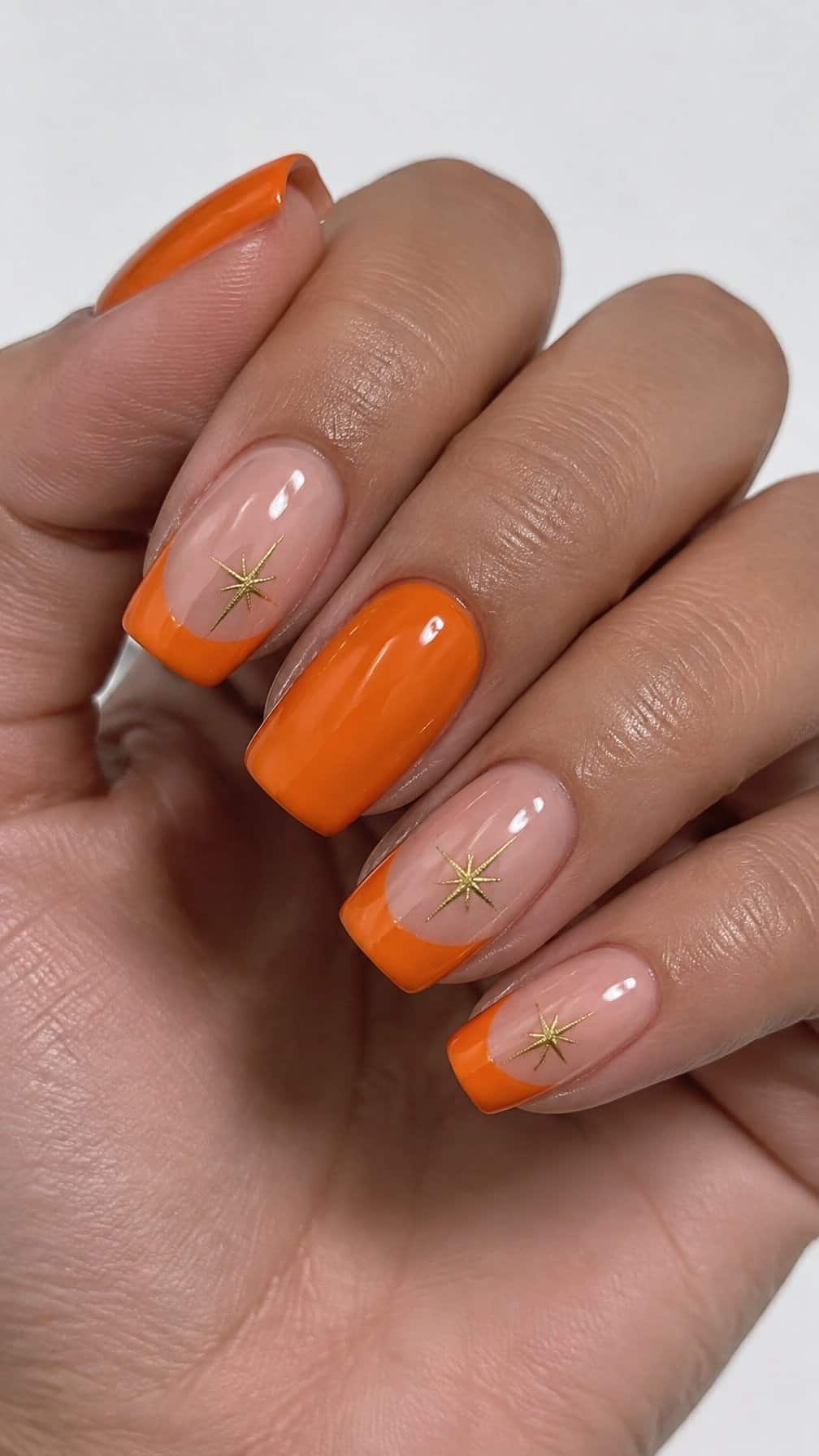 Orange French tip nails and small gold starburst designs