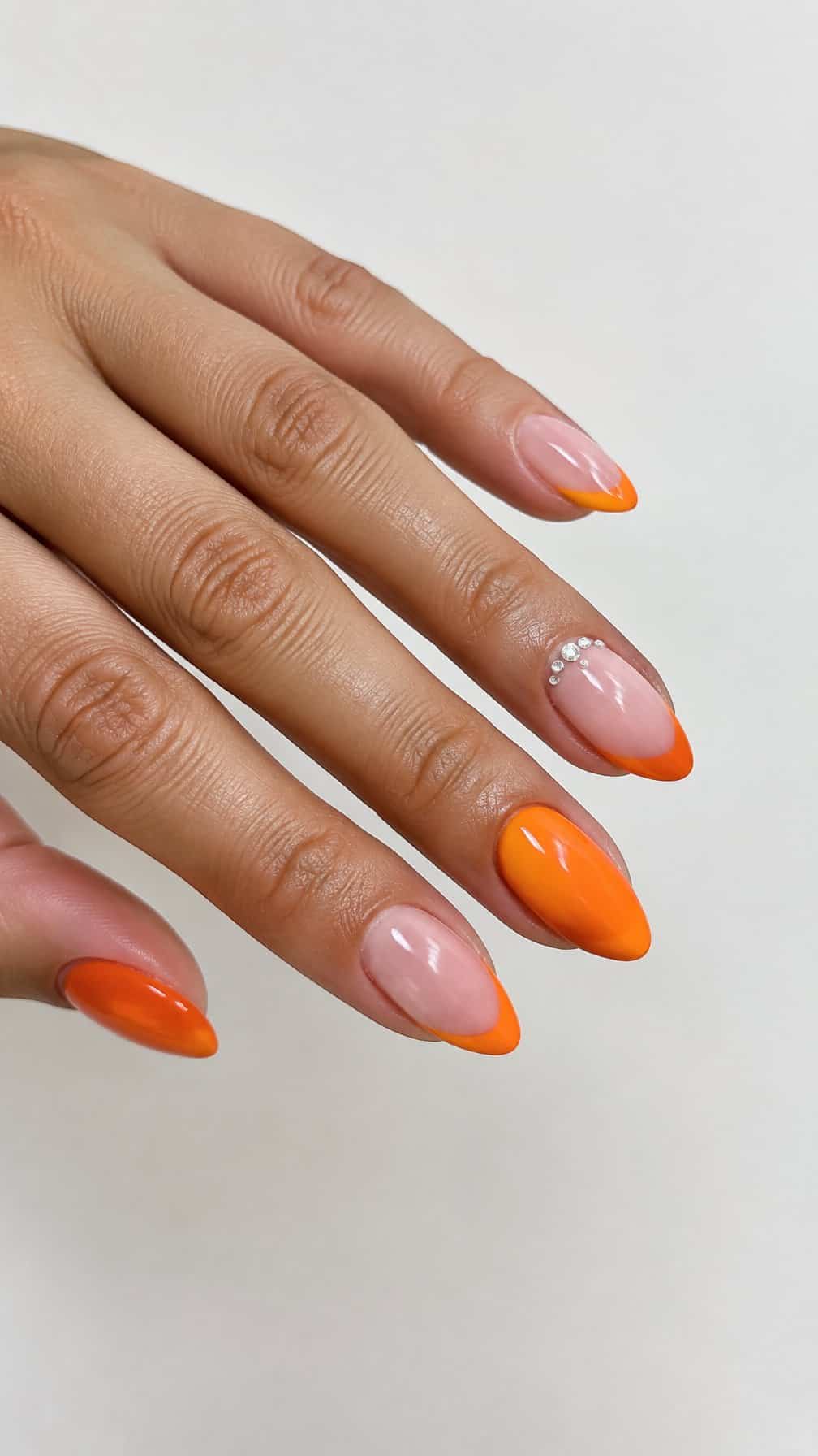 Glossy orange French-tip nails and small rhinestones near the cuticles
