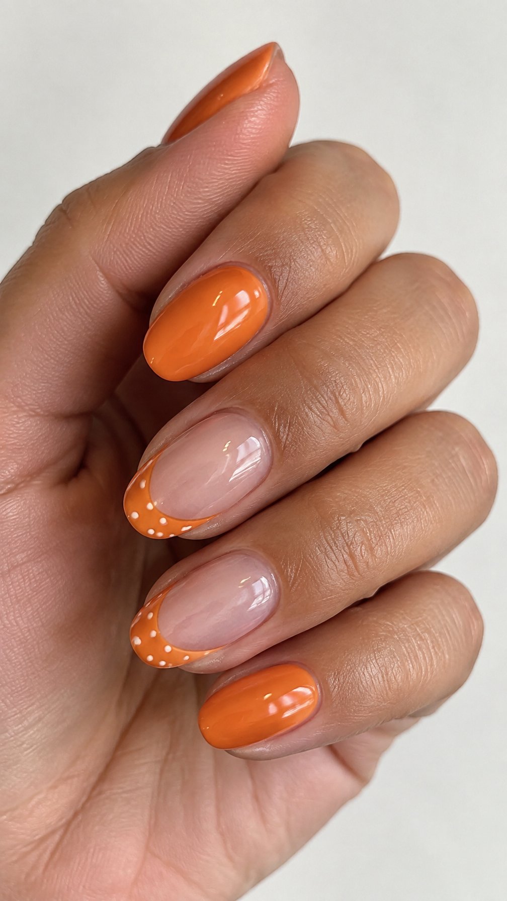 Glossy orange French-tip nails and small white dots