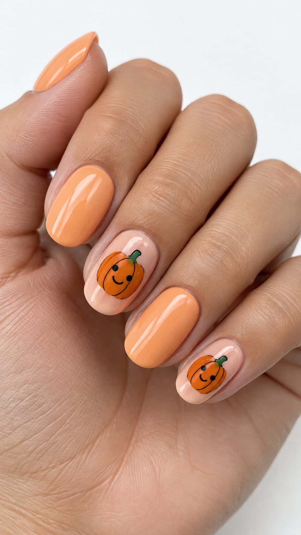 Glossy peach nails and small smiling pumpkin designs on several fingers