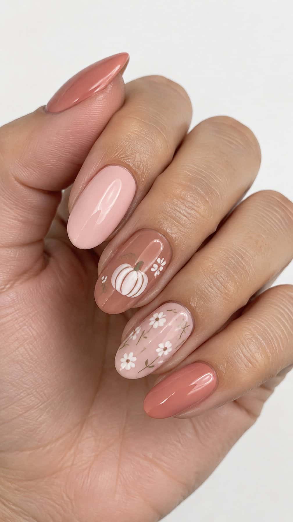 Pink gel nails decorated with white pumpkin and floral designs