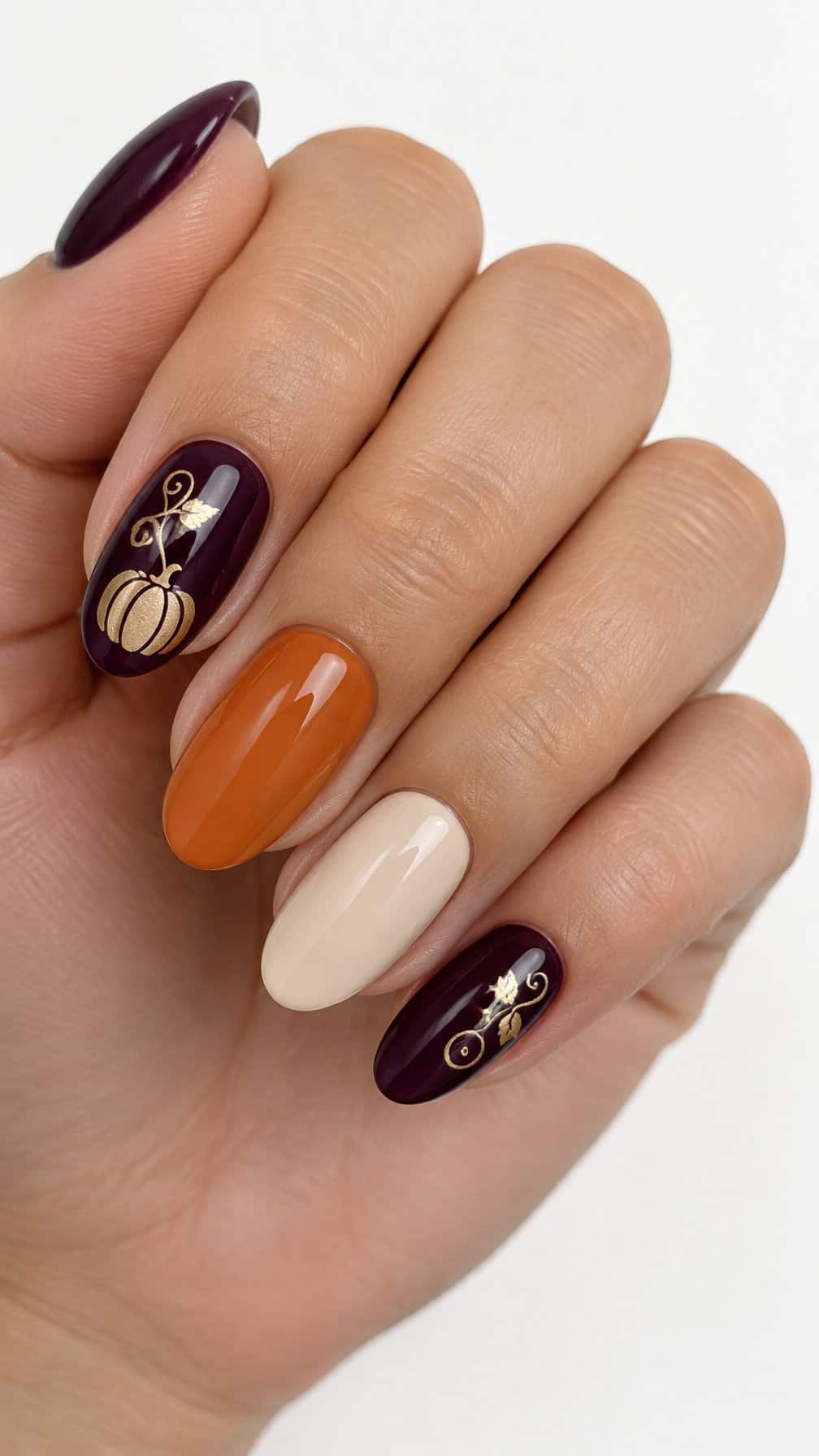 Glossy plum, pumpkin-orange, and pale nails decorated with small gold pumpkin vines