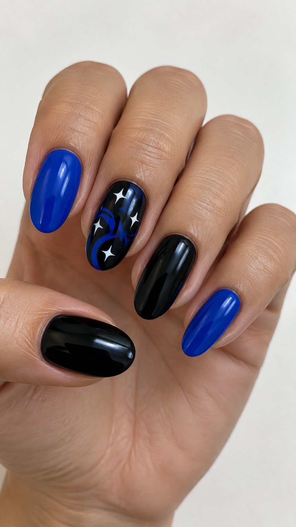 Glossy black and cobalt blue nails, including white star and swirl designs on one nail