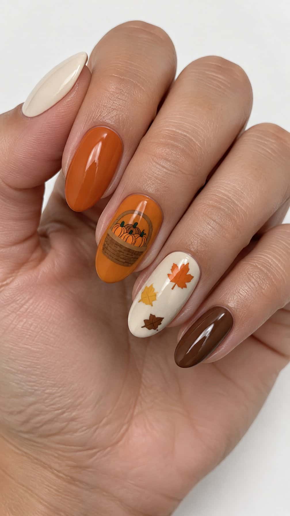 Glossy autumn-themed manicure featuring pumpkins, a basket, falling leaves, and solid warm-colored nails