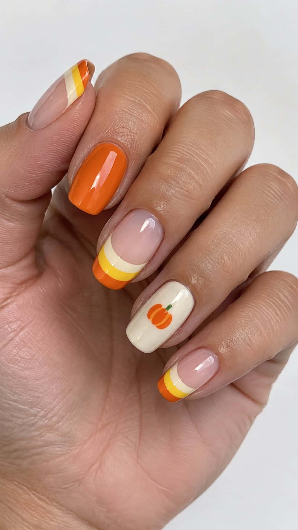 Glossy pumpkin orange, ivory, and yellow French-tip nails and small pumpkin designs