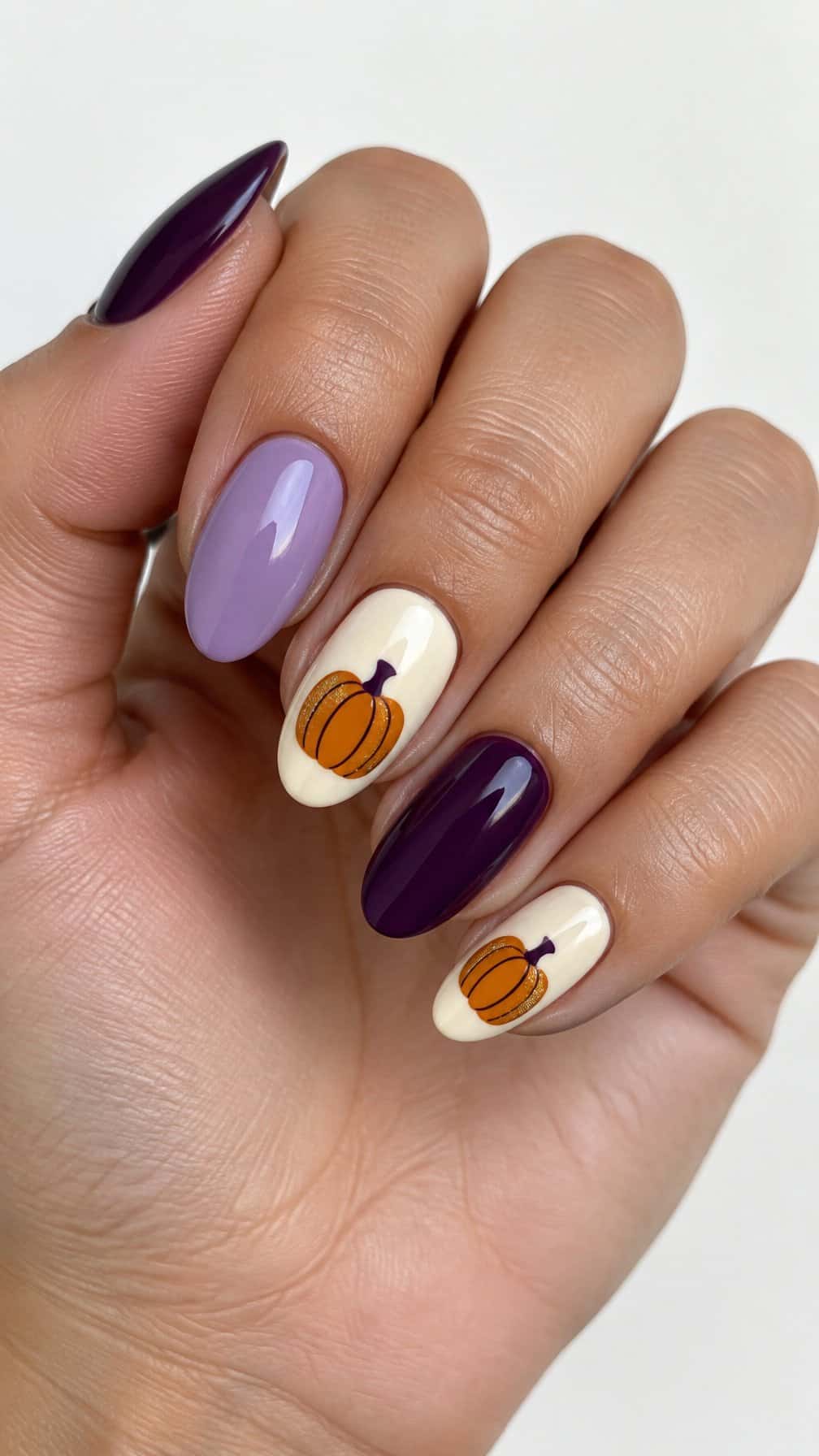 Glossy purple Halloween-themed nails featuring small orange pumpkin designs