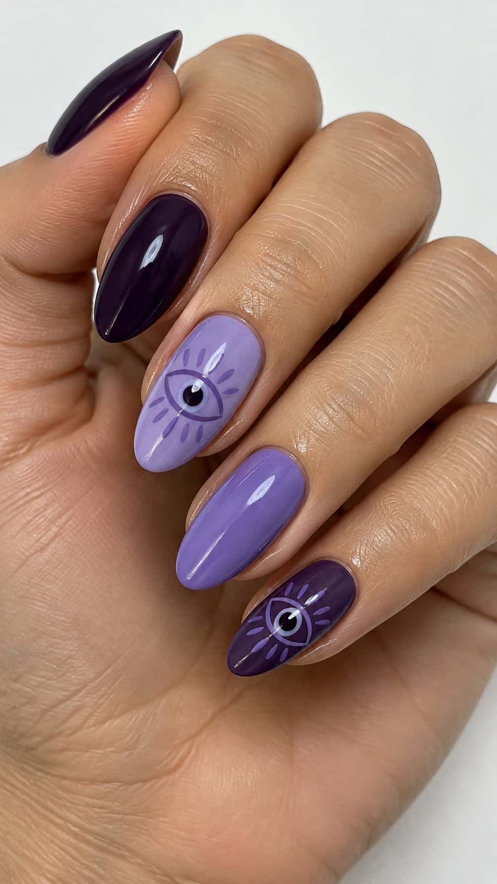 Glossy purple manicure featuring mystical eye designs on several nails