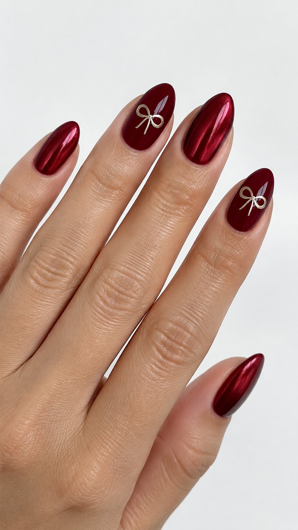 Deep ruby red glossy nails and small metallic bow designs on two accent nails