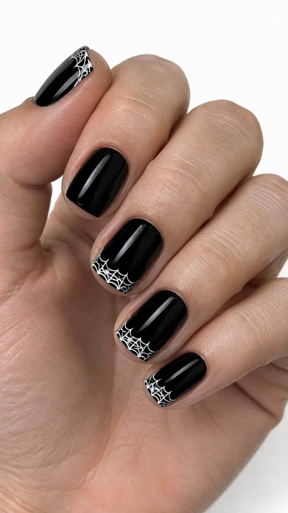 Short glossy black nails, some decorated with white spider-web French tips