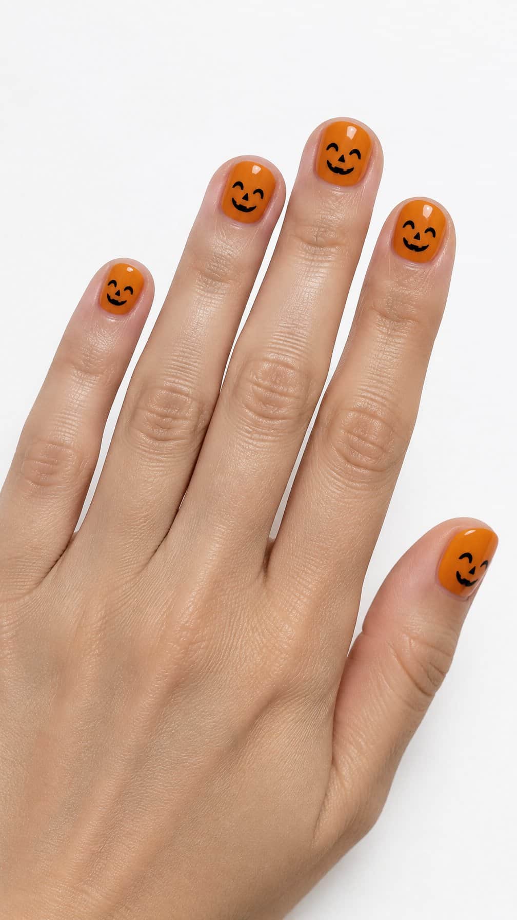 Short round orange nails decorated with tiny smiling pumpkin faces
