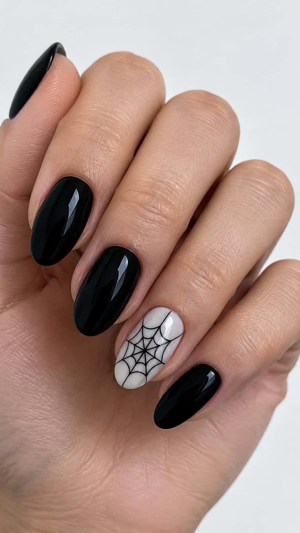 Glossy black gel nails and one pale accent nail painted with a black spider web