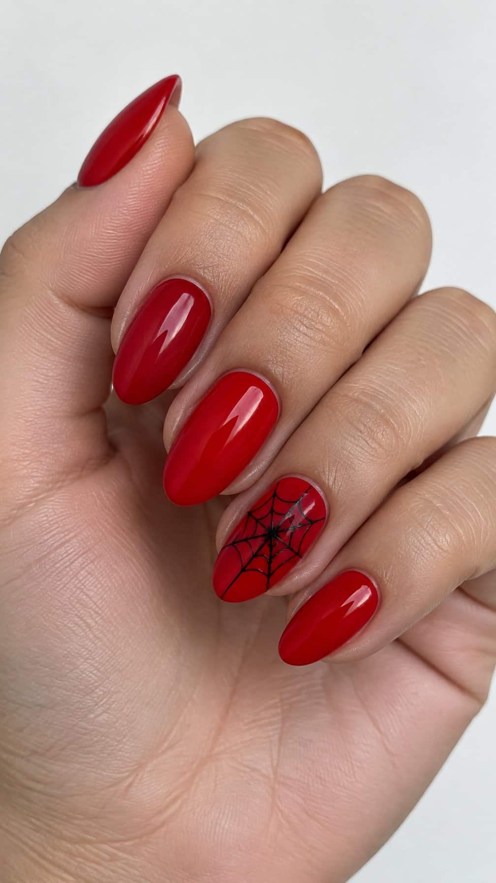 Glossy red nails and a black spider web design on the ring finger