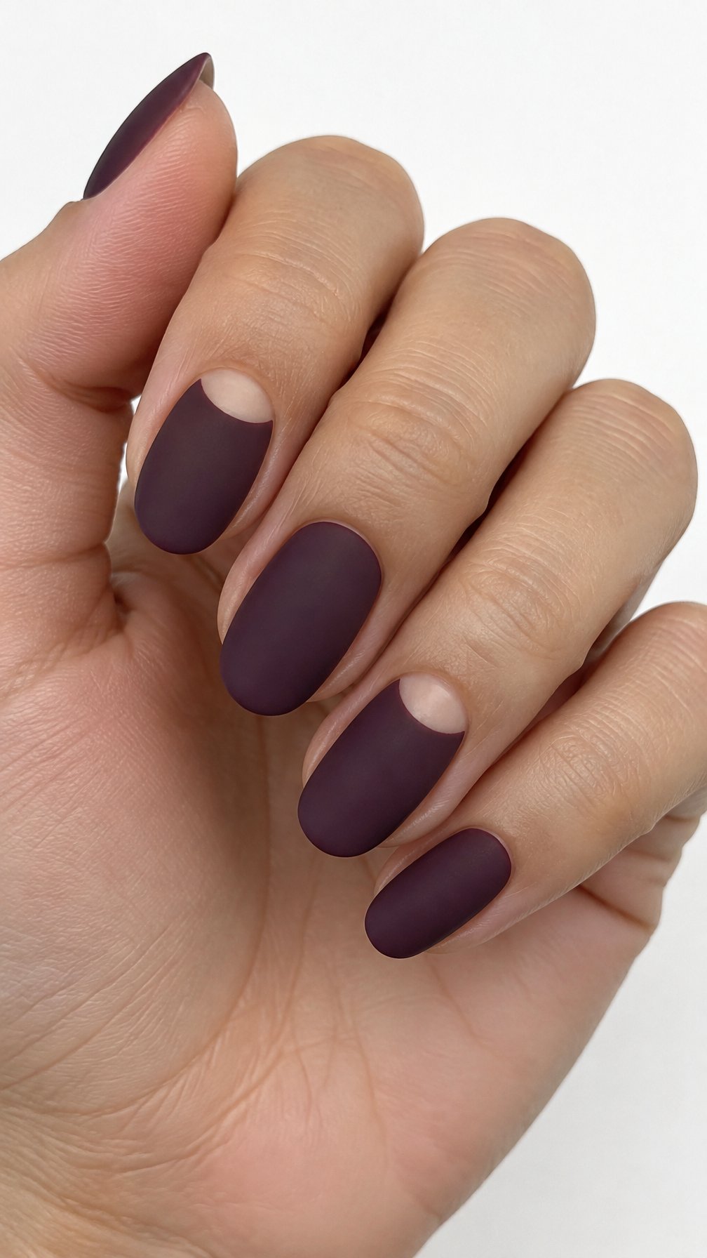 Short plum-colored manicured nails featuring bare half-moon shapes near the cuticles