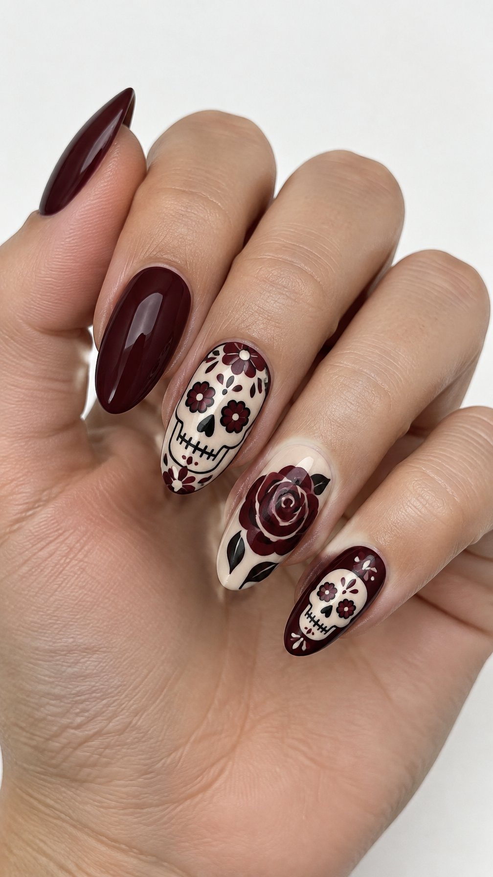 Glossy deep burgundy nails, rose designs, and small skull accents