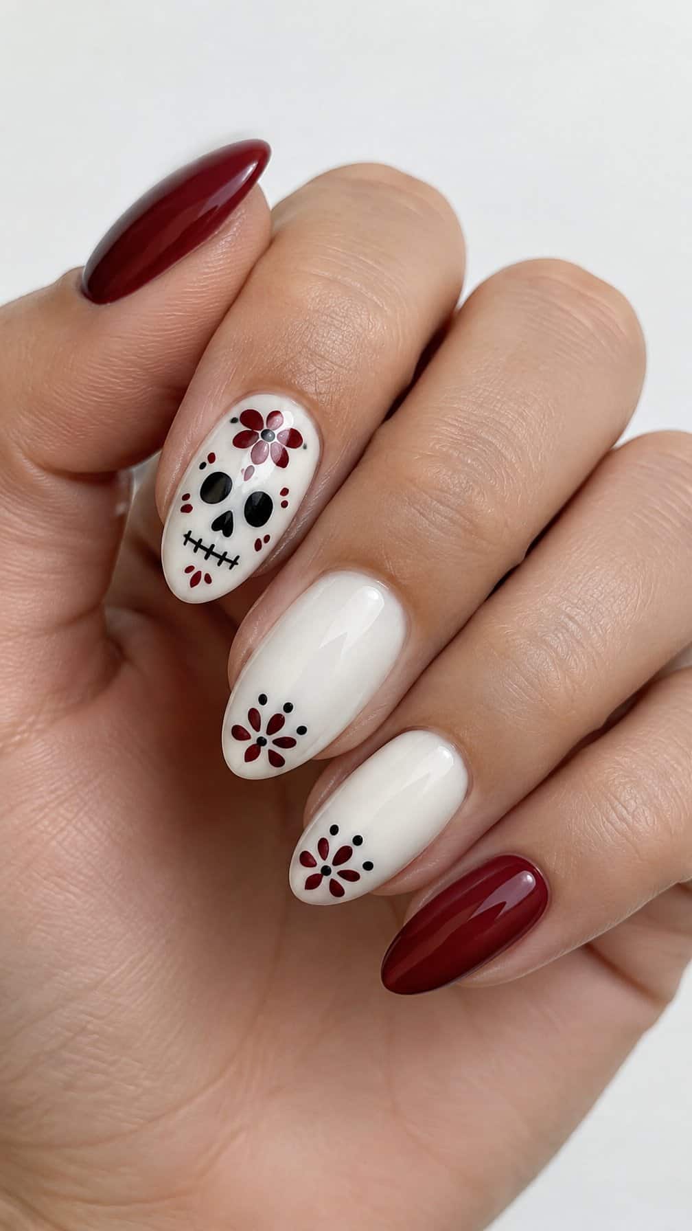 Glossy burgundy and white nails, including a white sugar skull design on one accent nail