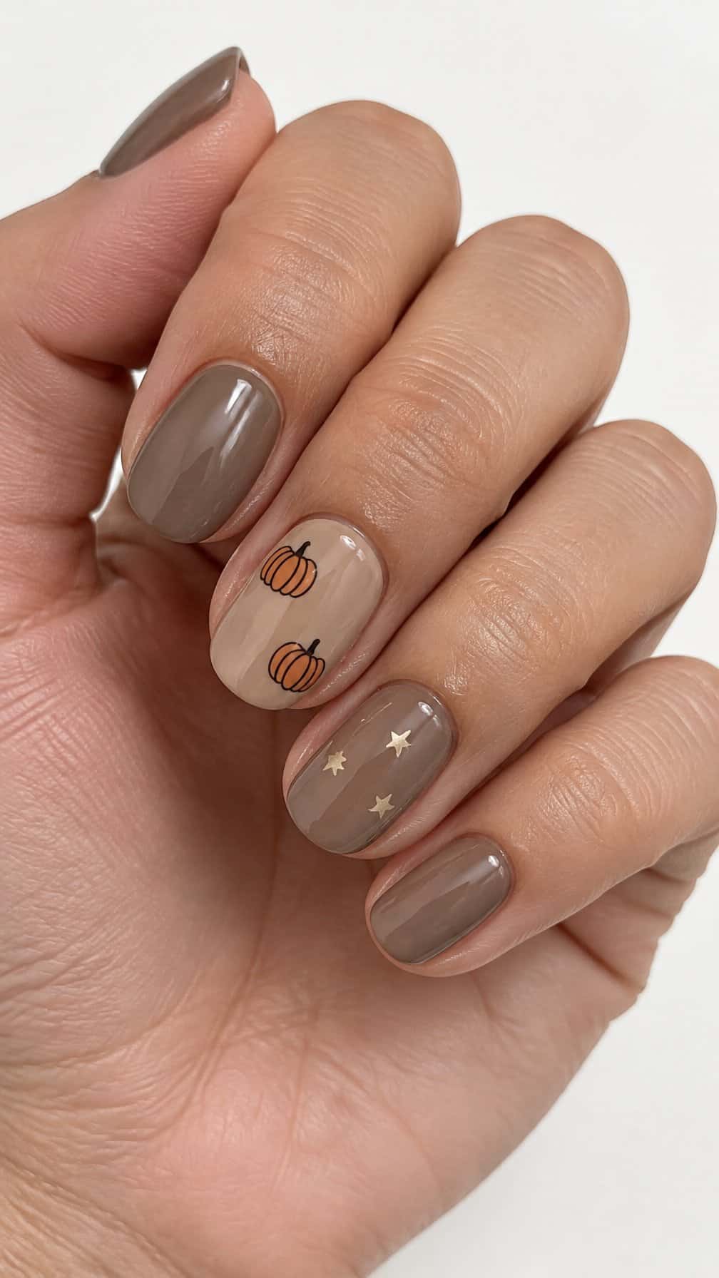 Glossy taupe nails, tiny pumpkin designs, and small star accents