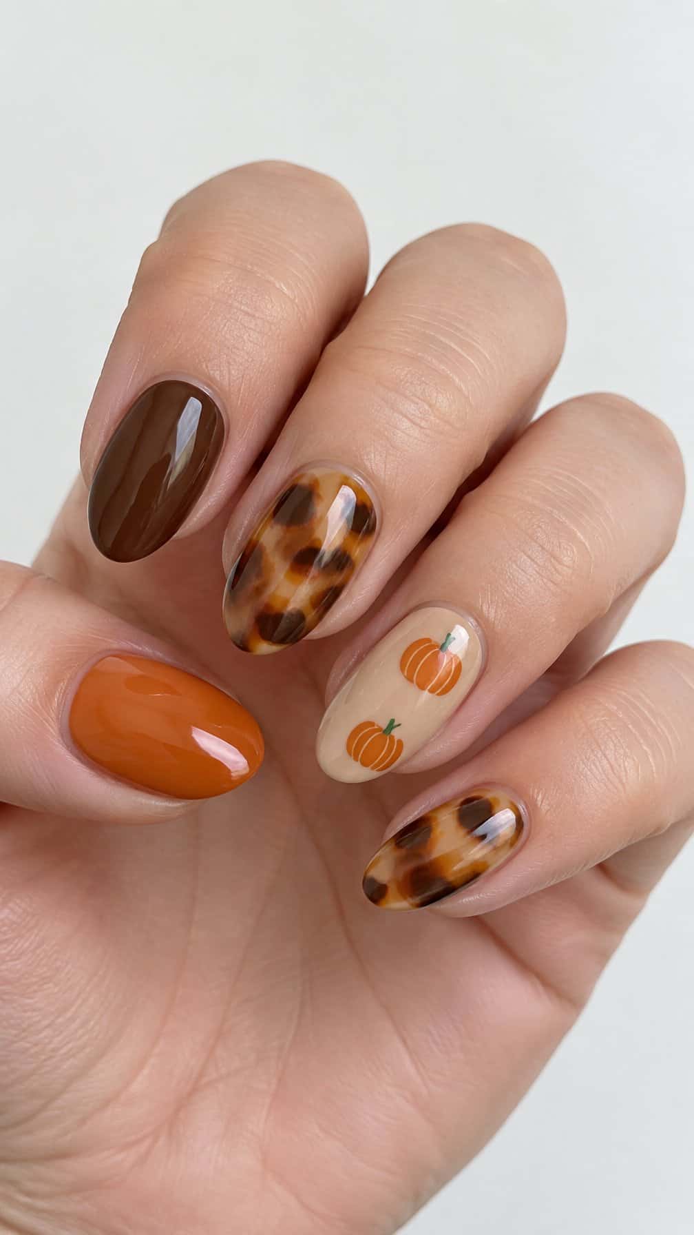 Glossy autumn gel nails featuring tortoiseshell patterns, orange pumpkins, and solid coordinating colors