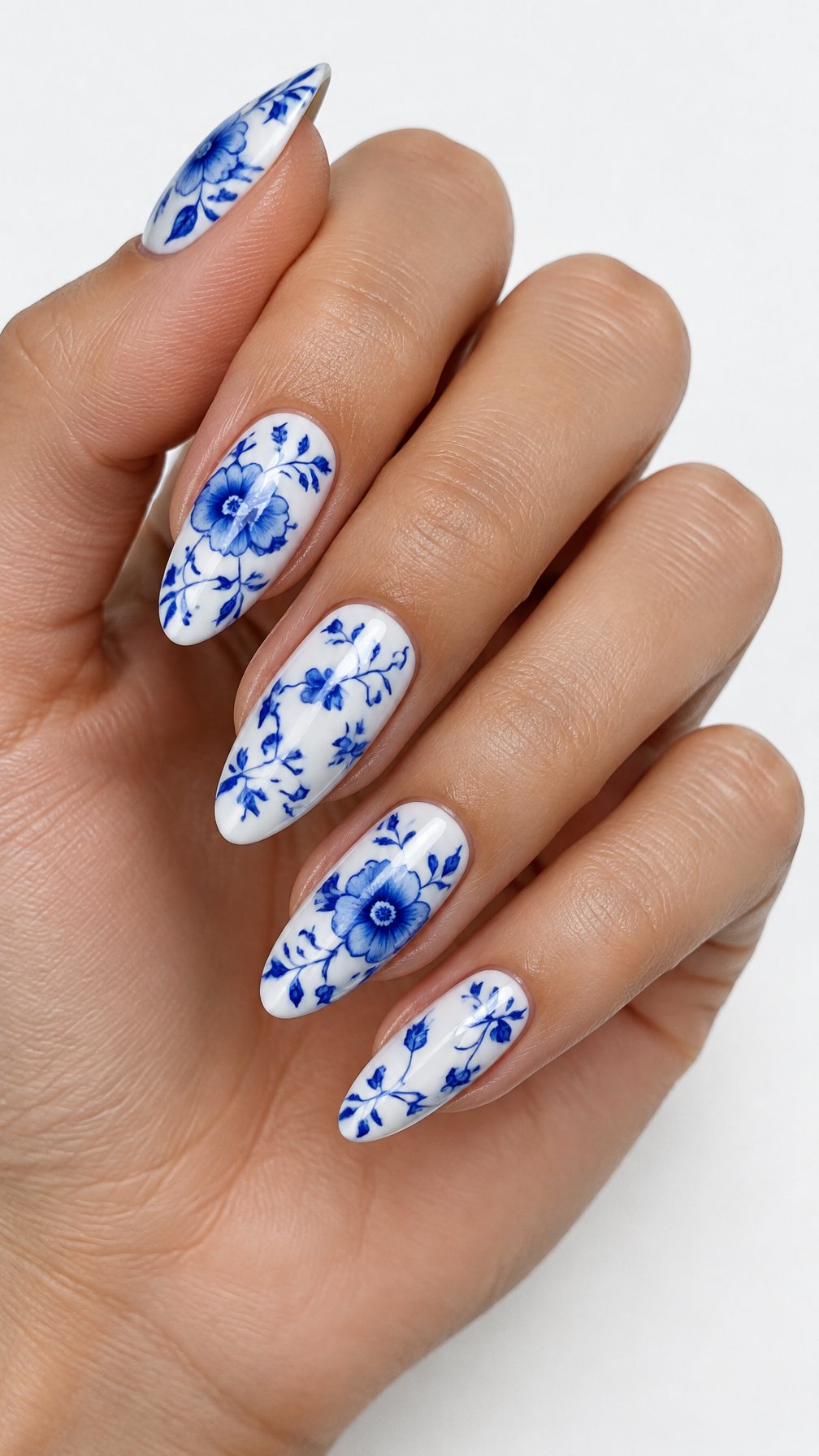 A single hand with glossy white nails decorated with intricate blue floral vines on a white background.
