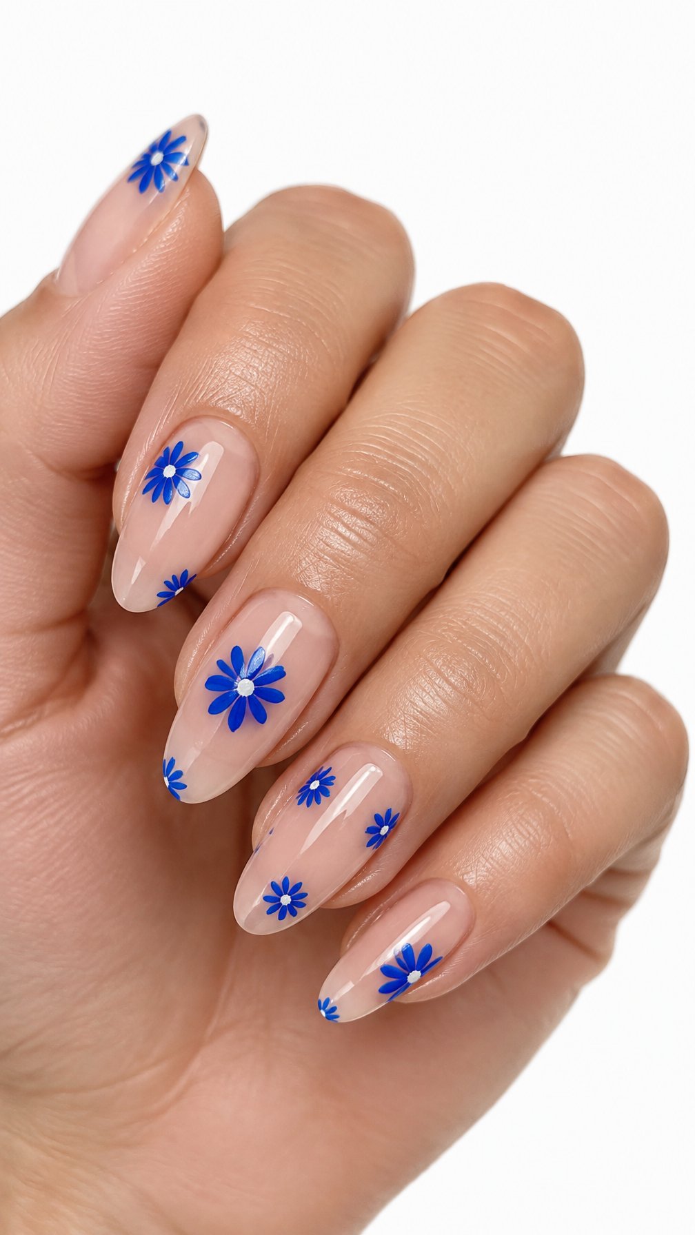 A single hand with sheer nude nails decorated with glossy cobalt blue daisy flowers on a white background.