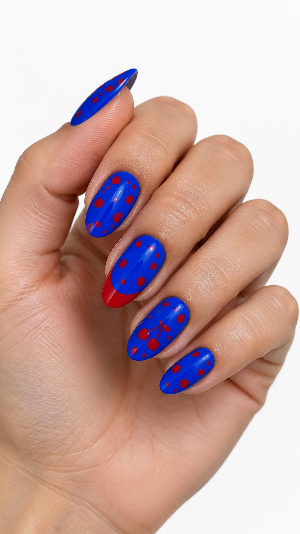 A single hand with glossy cobalt blue nails decorated with cherry red polka dots and accent details on a white background.