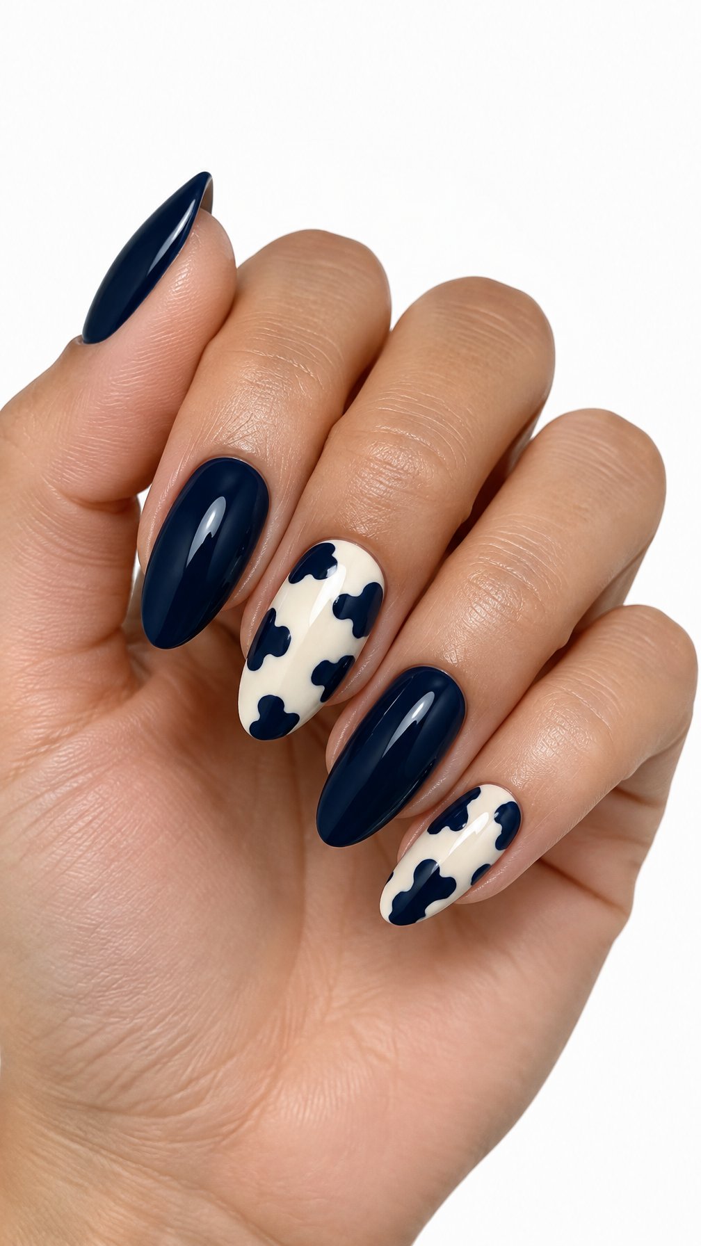 One hand with glossy midnight blue and cream cow print manicured nails against a white background.
