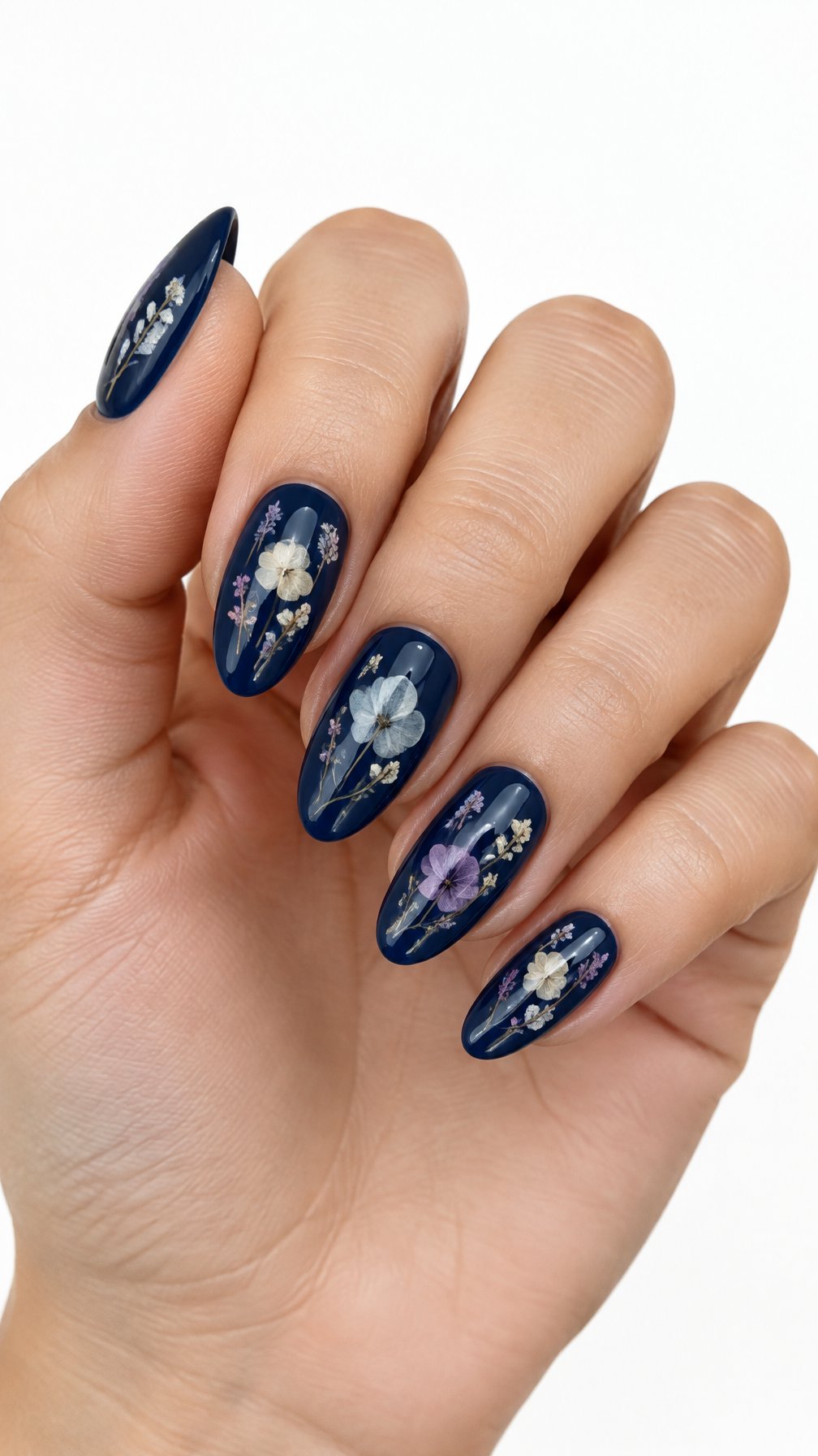 A single hand with glossy midnight blue nails decorated with delicate pressed flowers rests against a white background.