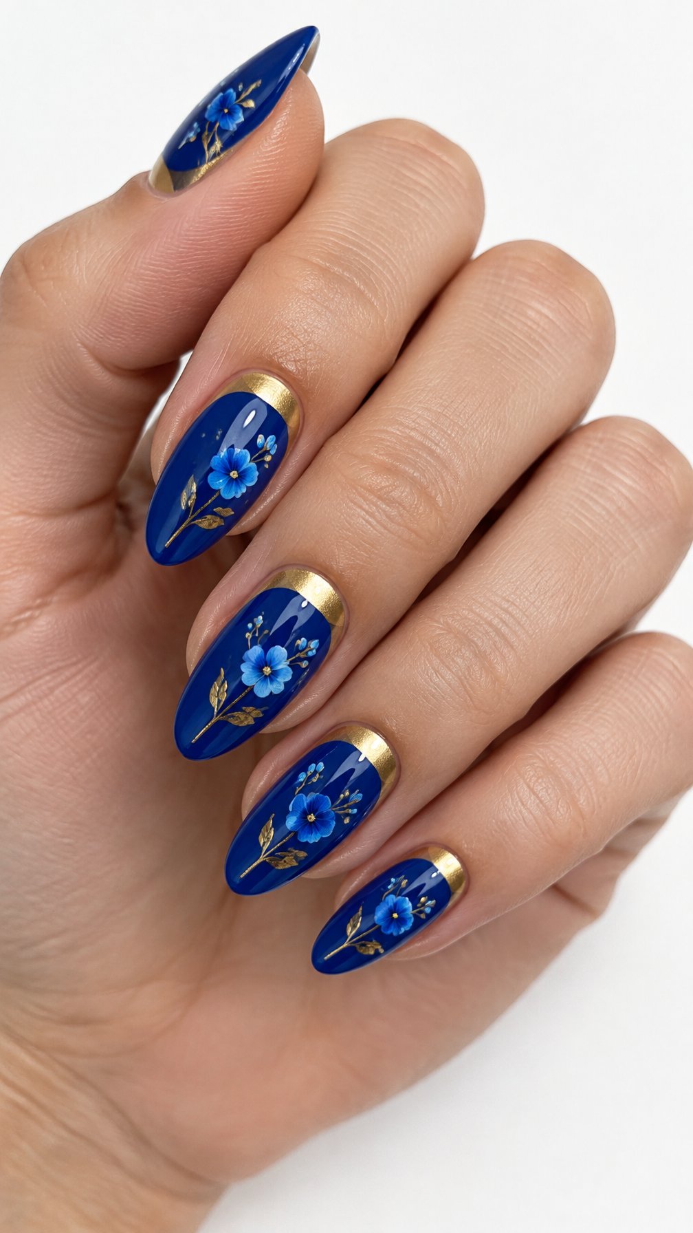 A single hand with cobalt-blue and gold floral half-moon manicured nails against a white background.