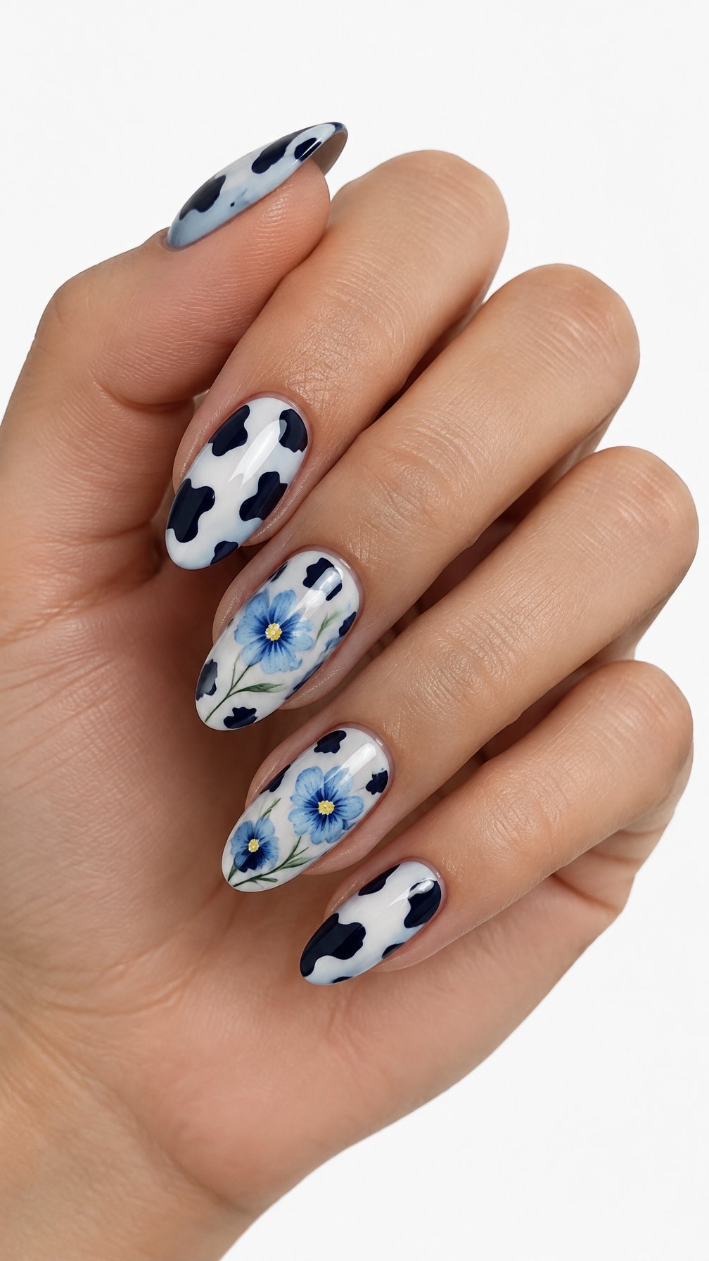 A single hand with glossy almond-shaped nails featuring blue flowers and cow-print patterns on a white background.