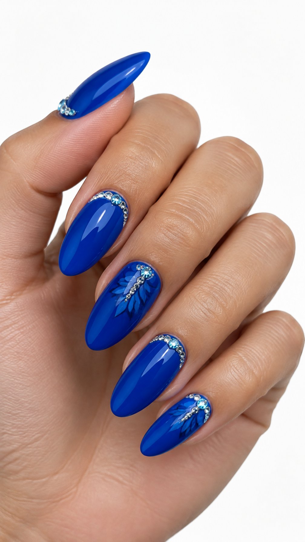A single hand with glossy cobalt blue almond-shaped nails decorated with small crystals near the cuticles on a white background.