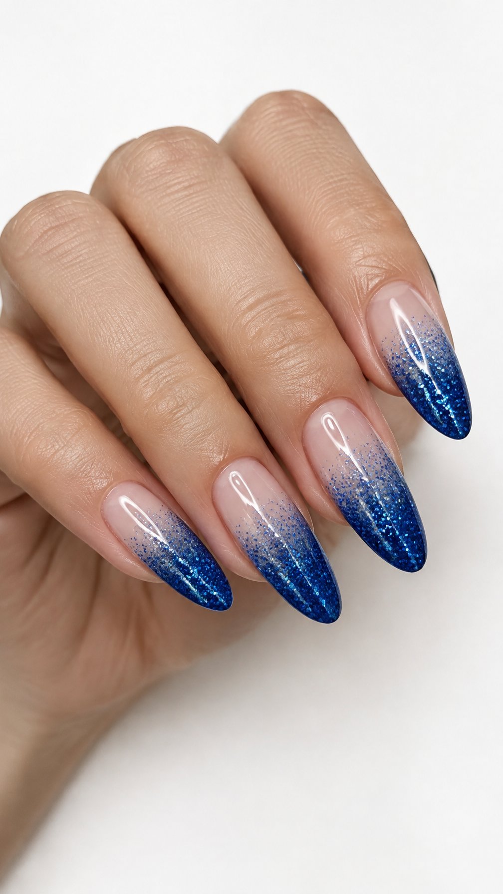 A single hand with sapphire blue glitter ombré almond-shaped nails against a white background.